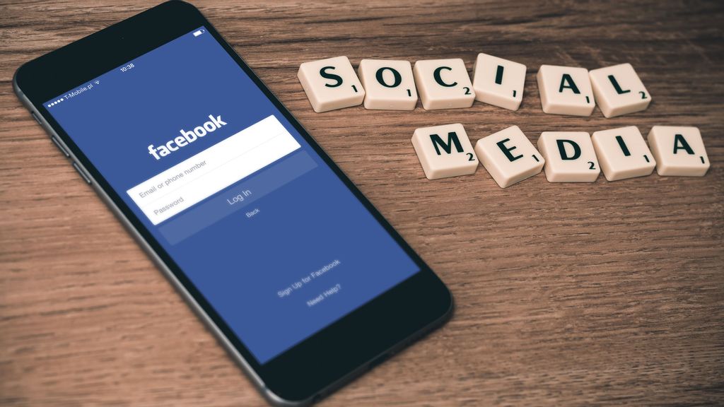 Phone with Facebook log-in display and social media scrabble tiles are arranged next to it. In this day and age of digital advancement, social media platforms have led to the creation of different alternate professions. (Frimbee/Unsplash) 